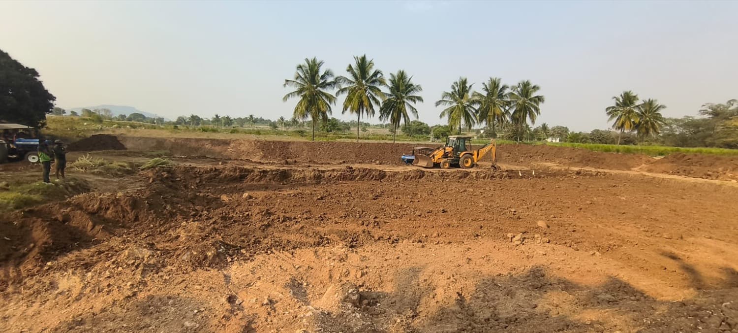 An excavator digging a new farm pond on red Karnataka soil