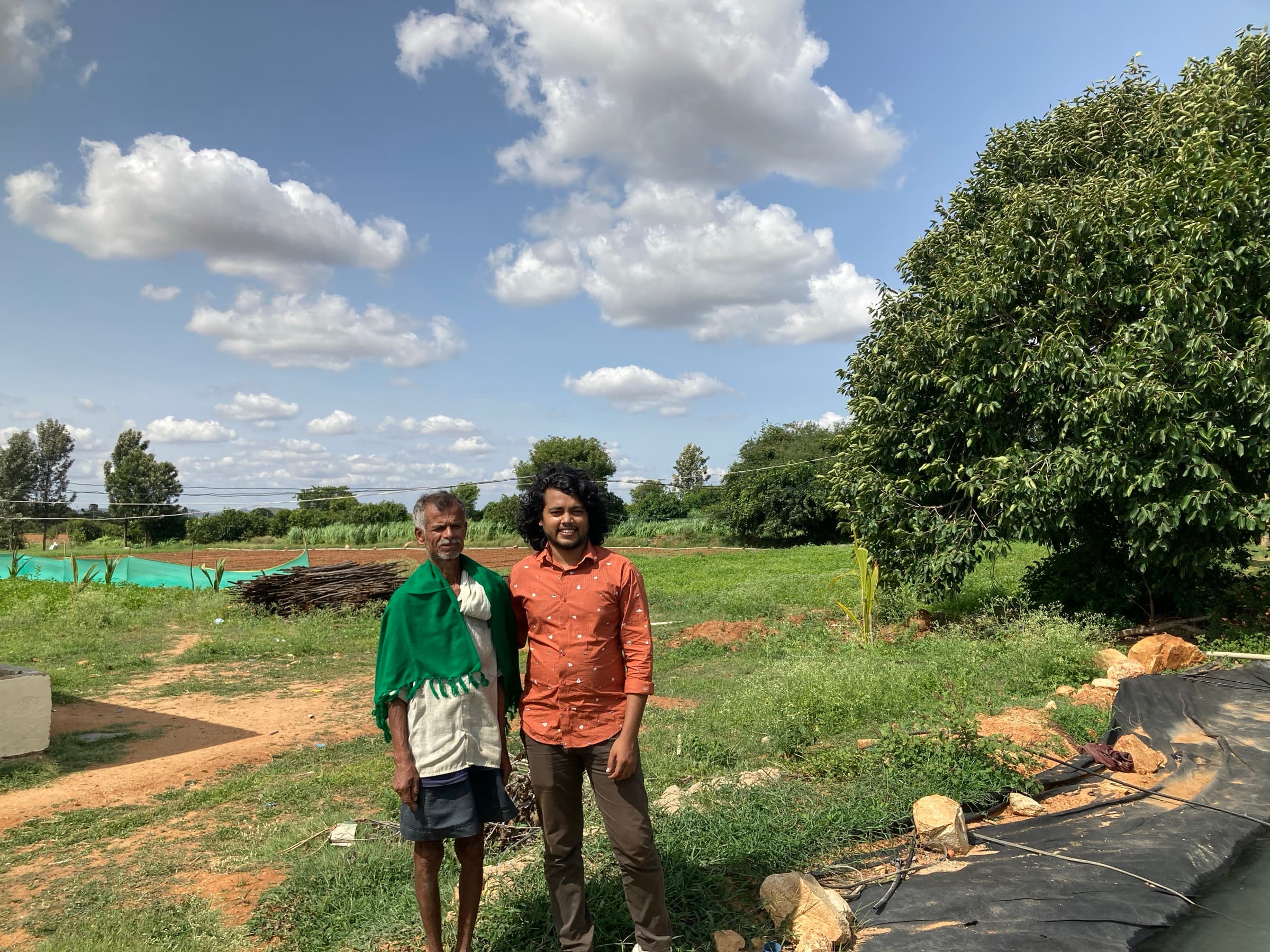 A HasiruAqua founder and a farmer stand together beside a freshly lined, newly stocked pond under a big sky
