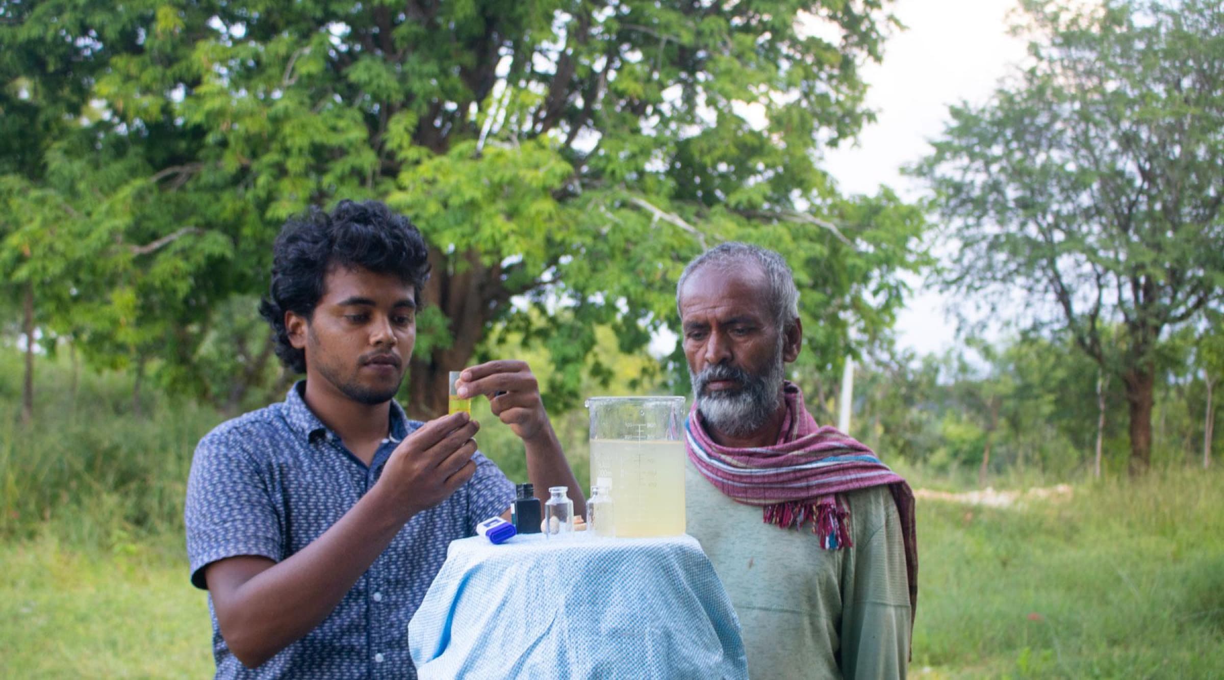 A HasiruAqua founder holds a water sample up to the light while a farmer watches